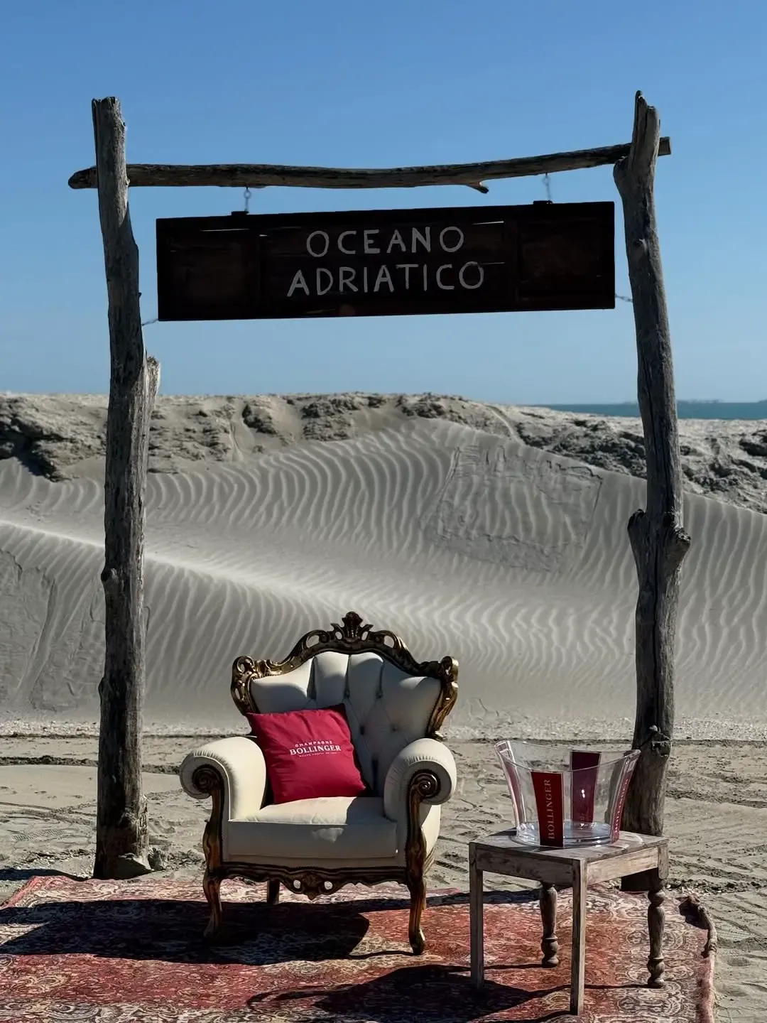 Poltrona vintage sulla spiaggia con cuscino Bollinger e cartello Oceano Adriatico
