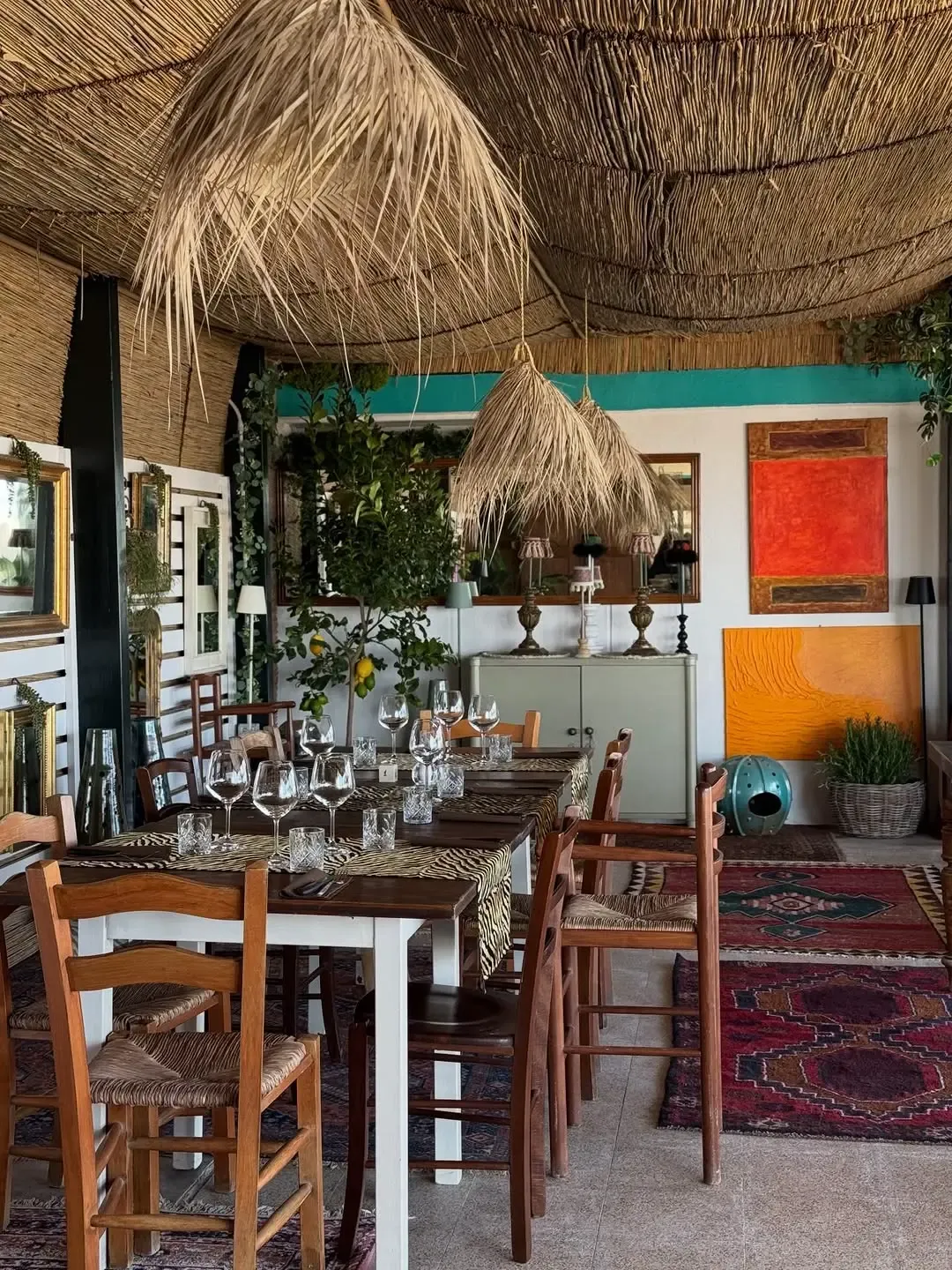 Sala interna con soffitto in paglia, lampade intrecciate, quadri colorati e piante tropicali