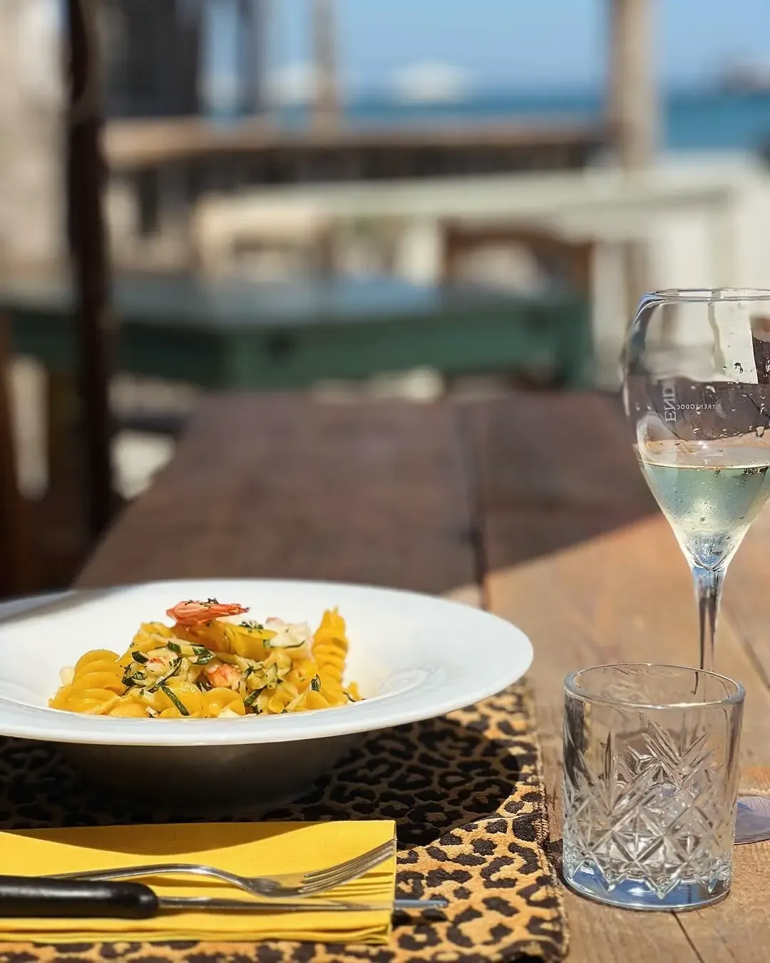 Fusilli con gamberetti e zucchine su piatto bianco con vista mare, placca leopardata