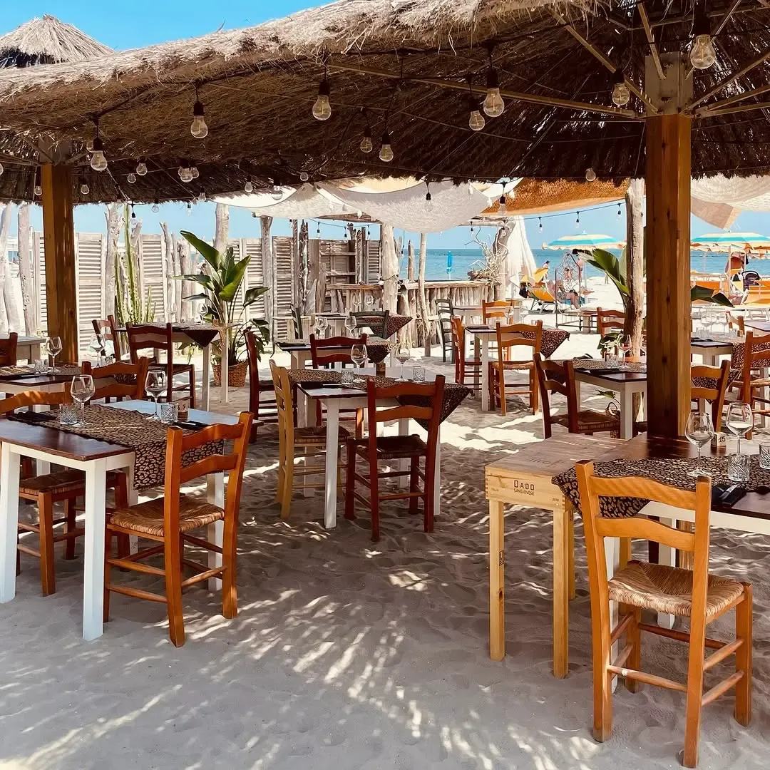 Ristorante all'aperto con tetti in paglia e tavoli sulla sabbia