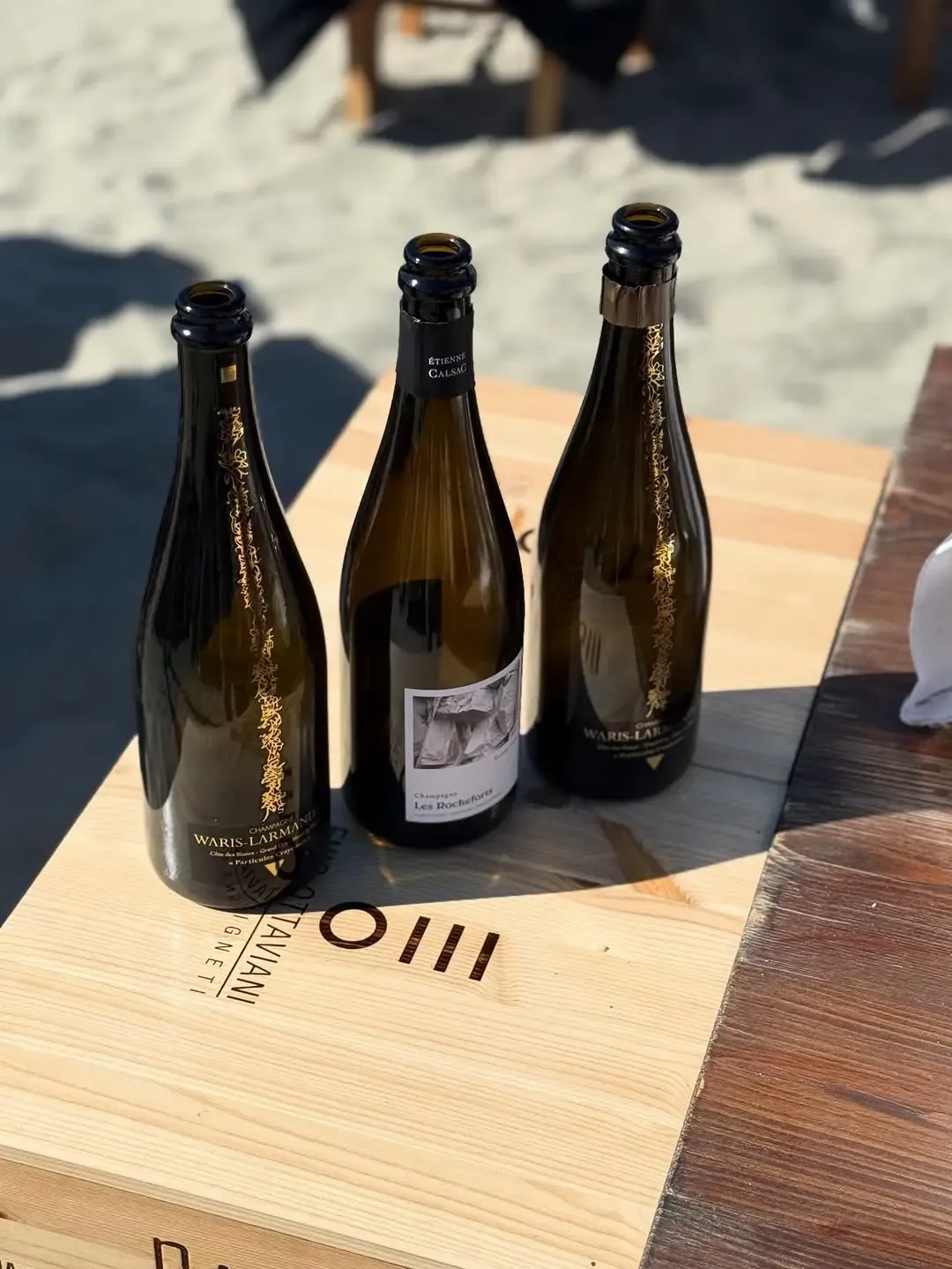 Tre bottiglie di champagne Waris-Larmandier e Calsac su cassa in legno in spiaggia